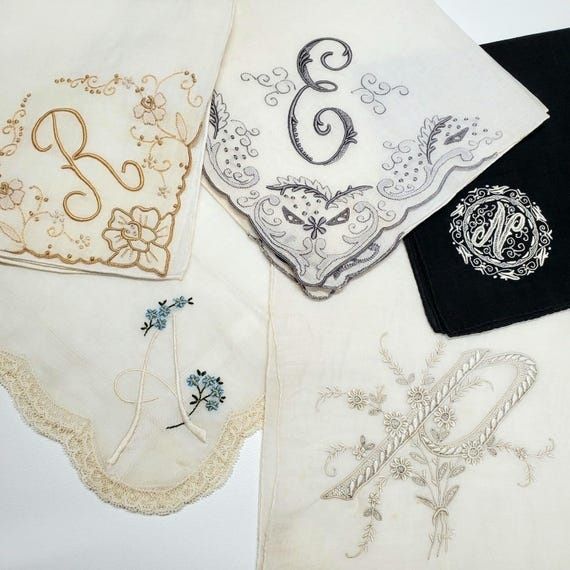 Äldre linnetextilier med broderade monogram, blommor och spetskanter